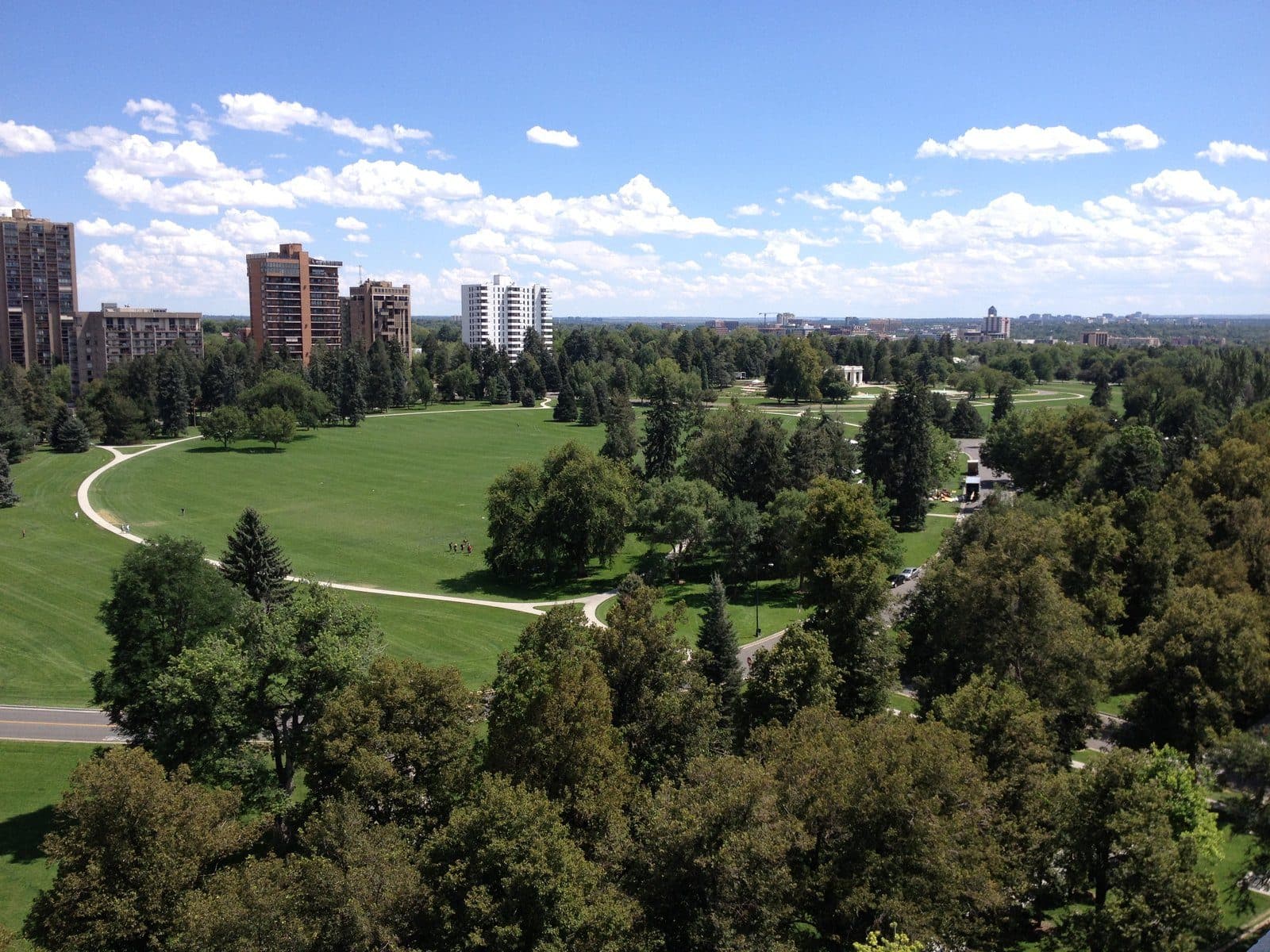 An elevated summer view over Cheesman Park's lawns and tree canopy toward the Denver skyline