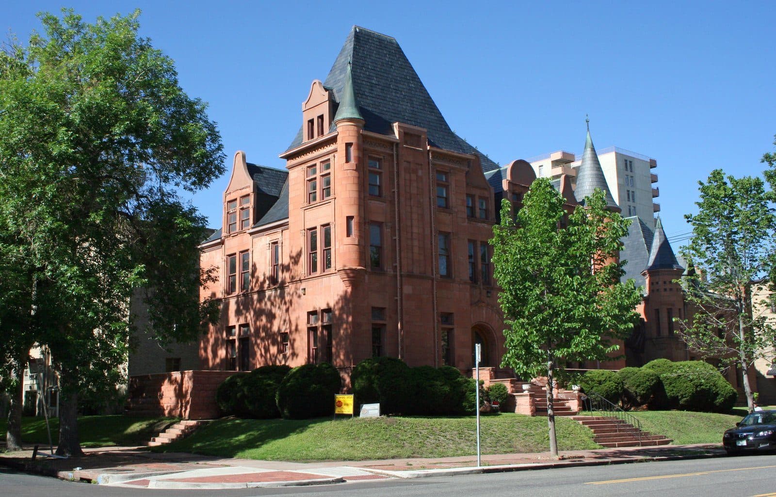 A grand red-sandstone historic mansion on a tree-lined corner near Cheesman Park