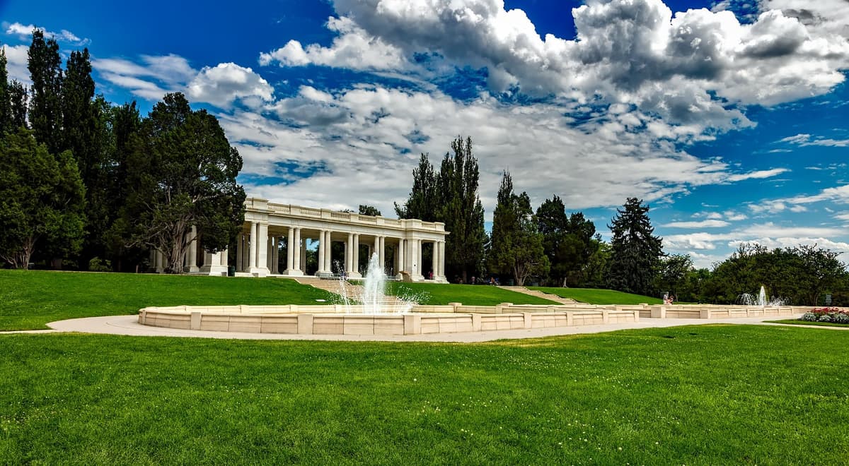 The white marble pavilion and fountain at Cheesman Park in Denver, with a wide green lawn under a blue sky