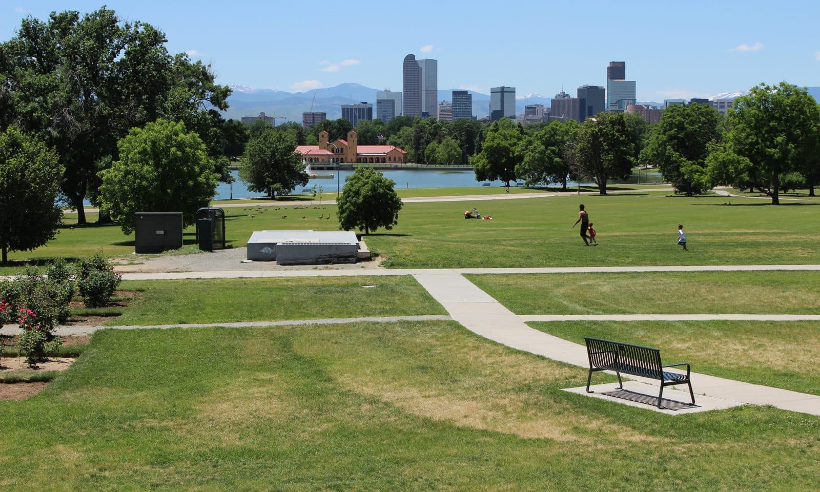 City Park on Park Hill's western edge — Ferril Lake and open lawns with the downtown Denver skyline and the mountains beyond