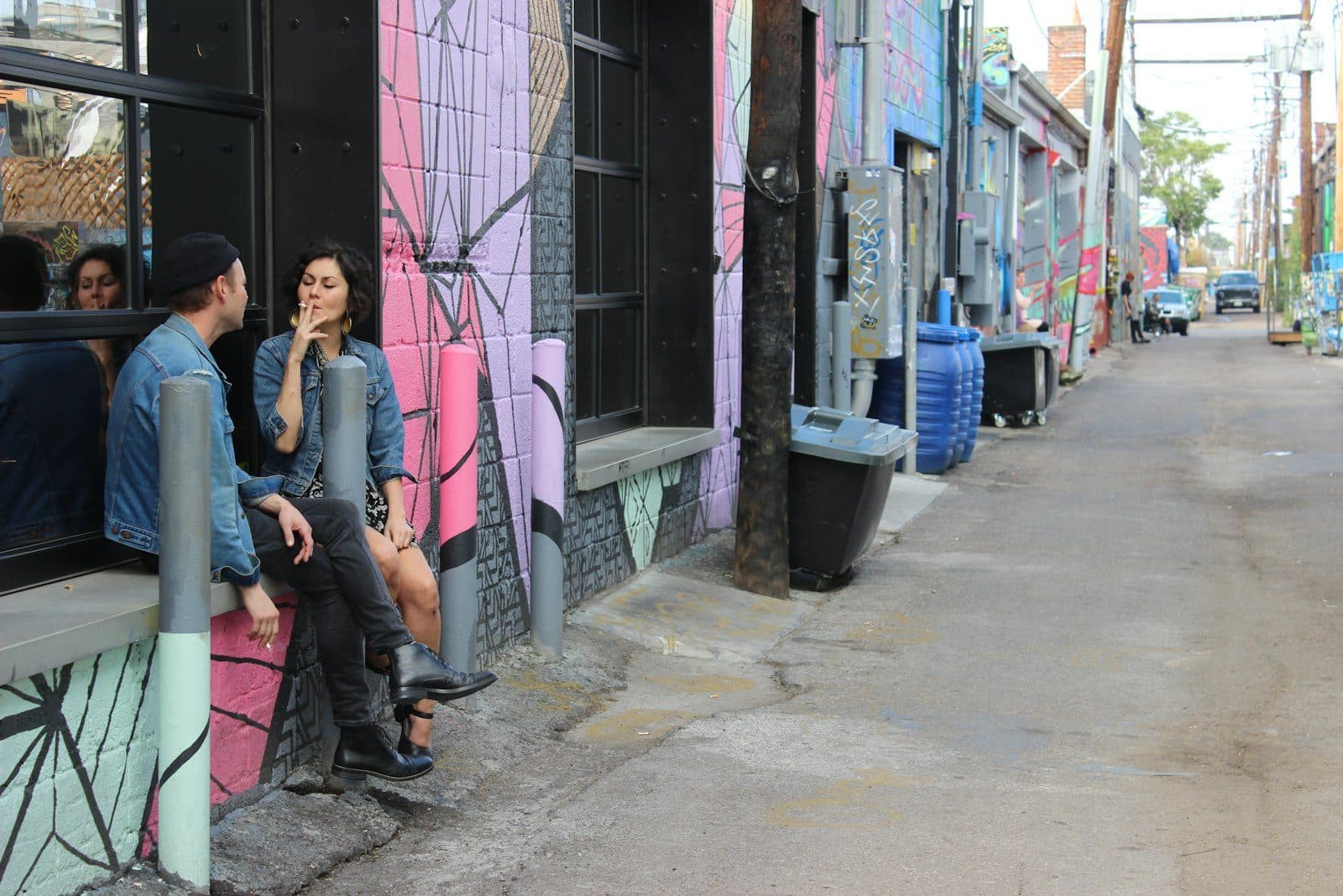 A mural-lined alley in RiNo, Denver, with people sitting against a painted warehouse wall