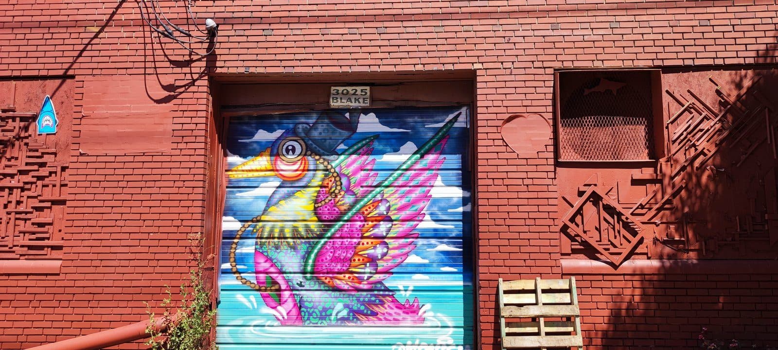 A colorful bird mural on a garage door set into a red-brick warehouse on Blake Street in RiNo