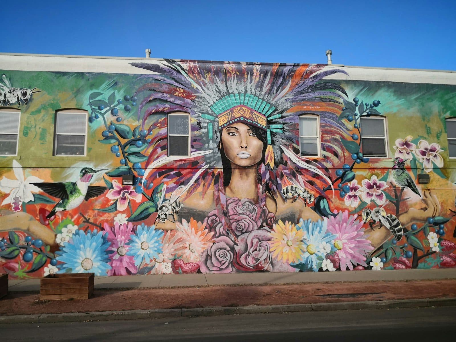 A photorealistic mural of a woman in a feathered headdress on a building in RiNo, Denver