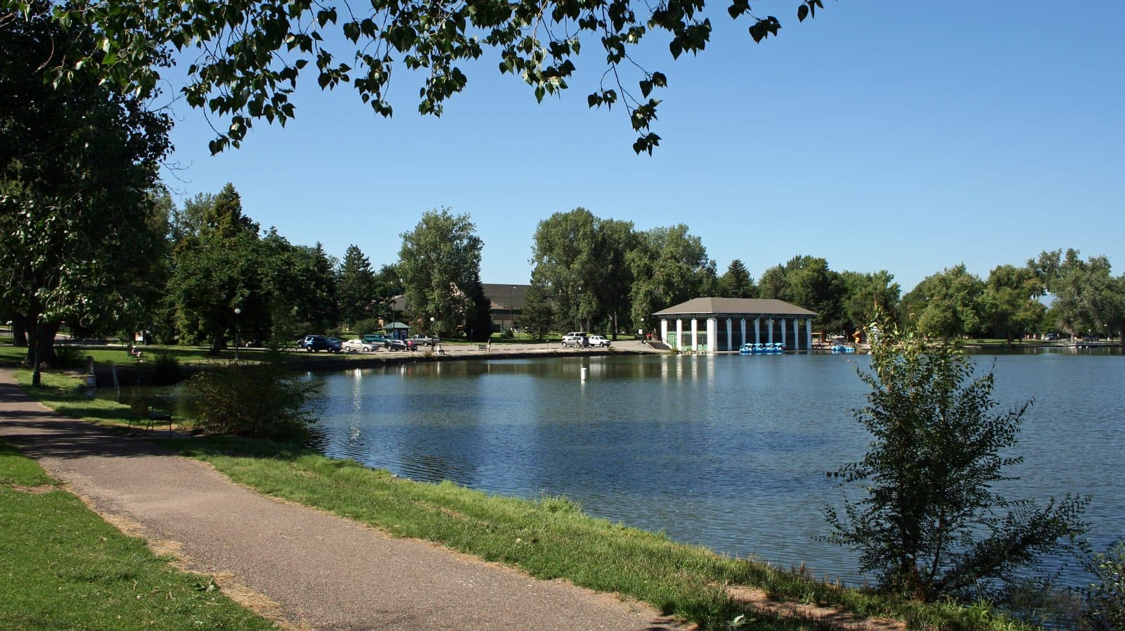 Smith Lake and the historic 1913 boathouse pavilion at Washington Park, with green lawns and a lakeside path in the foreground