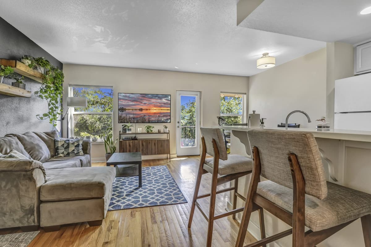 Wide view of the open living, kitchen and dining area with a Peloton bike and balcony door visible