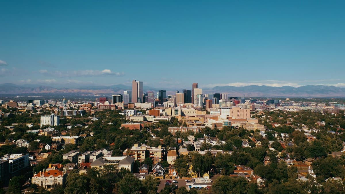 Downtown Denver rising from tree-lined neighborhoods with the Rocky Mountains on the horizon