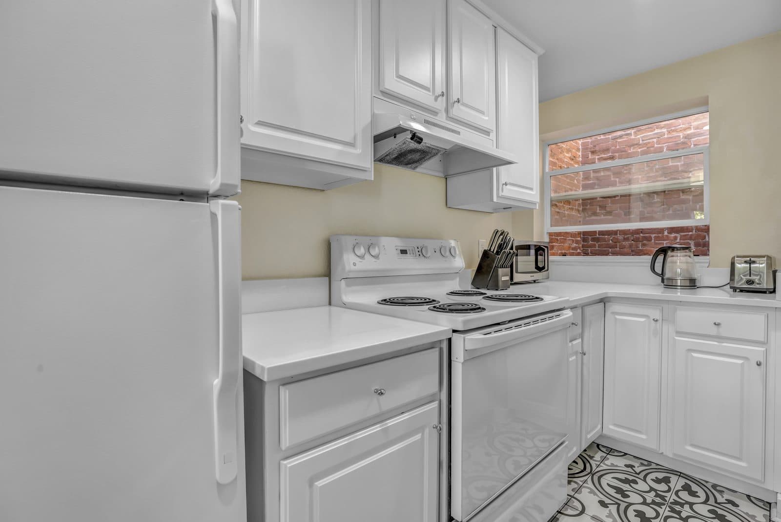 Kitchen with white cabinets, electric range and a window with an exposed brick view