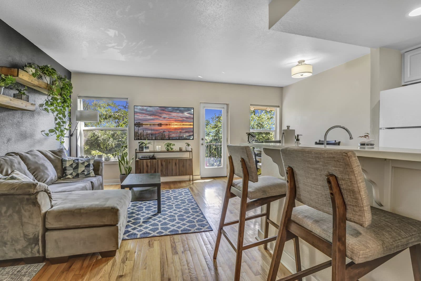 Wide view of the open living, kitchen and dining area with a Peloton bike and balcony door visible