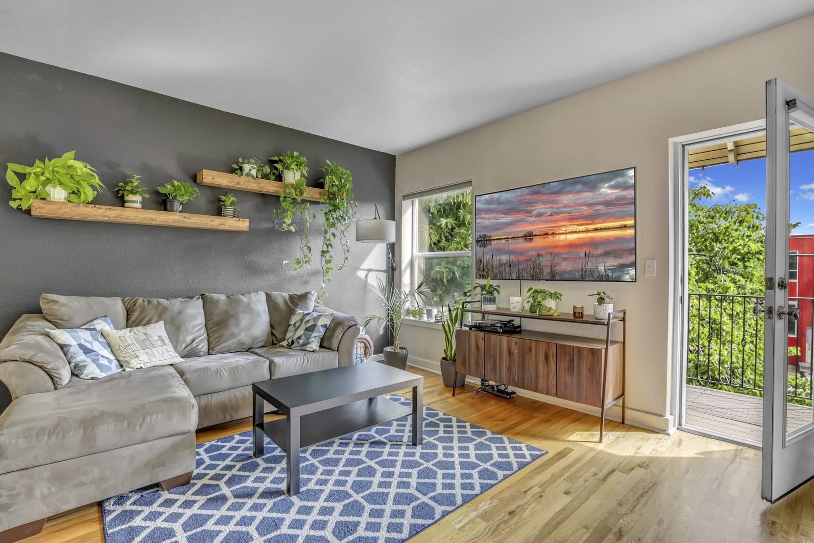 Living room with sectional sofa, gray accent wall and wood floating shelves with plants